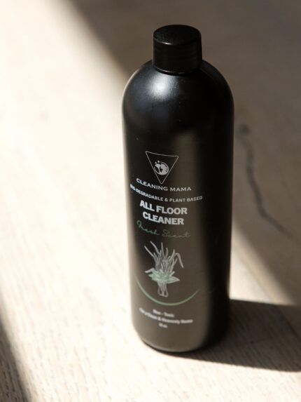 Cleaning Mama plant-based Fresh Scent All Floor Cleaner in a black bottle illuminated by sunlight on a wood floor.