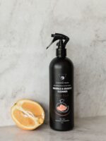 Cleaning Mama plant-based Fresh Scent Marble & Granite Cleaner in a black spray bottle beside a halved orange on a stone surface.