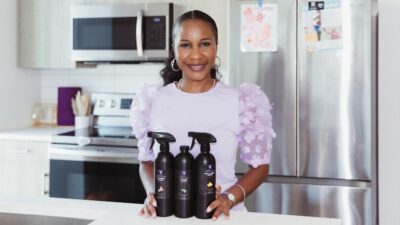Cleaning Mama founder, Mona Murahwa, is pictured in her kitchen. Three bottles of Cleaning Mama's small batch cleaners are on the counter in front of her,
