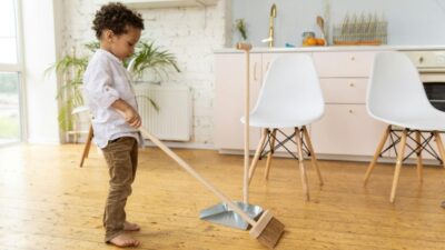 A little boy sweeps a hardwood floor to illustrate tips for cleaning with kids
