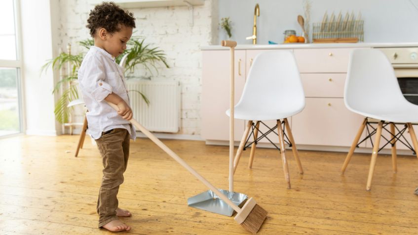 A little boy sweeps a hardwood floor to illustrate tips for cleaning with kids