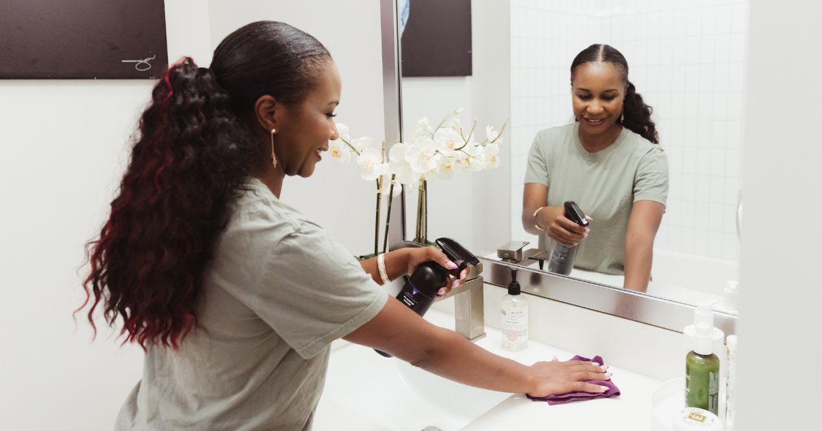 Cleaning Mama founder Mona Murahwa is pictured wiping down a bathroom counter with natural, non-toxic All Purpose cleaner.