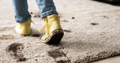 Child in yellow shoes tracking muddy footprints across a light-colored rug.