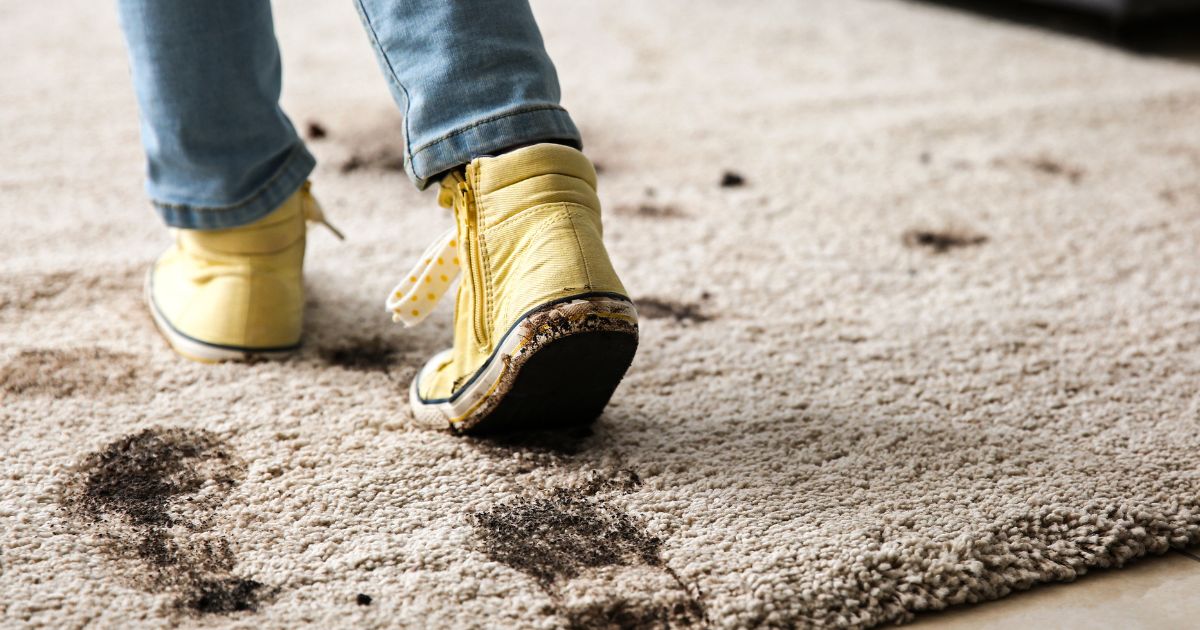 Child in yellow shoes tracking muddy footprints across a light-colored rug.