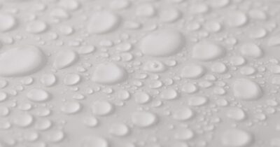 Close-up of water droplets beading across a smooth white surface, illustrating surface tension and how surfactants interact with water.