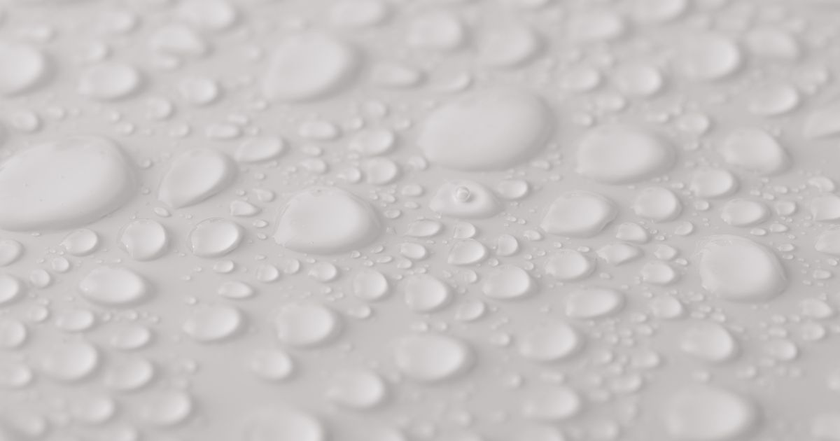 Close-up of water droplets beading across a smooth white surface, illustrating surface tension and how surfactants interact with water.