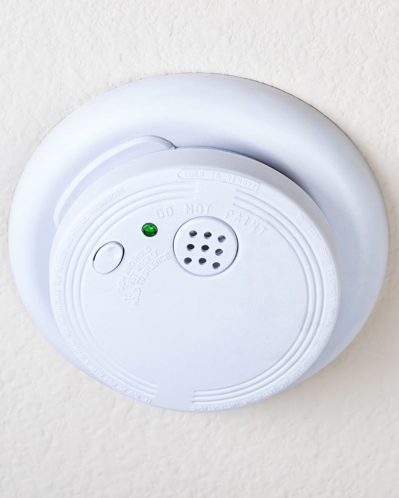 White smoke detector mounted on a ceiling during a seasonal home safety check