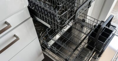Open dishwasher with empty upper and lower racks and a removable utensil basket in a modern kitchen.