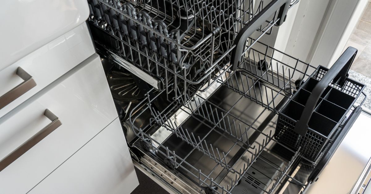 Open dishwasher with empty upper and lower racks and a removable utensil basket in a modern kitchen.